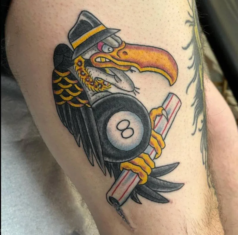 American Traditional color tattoo of a vulture wearing a fedora and gripping a black 8-ball and a red-and-white barber pole, on the thigh, by Franky Sharpz at Wailana Tattoo, Waikiki, Hawaii.