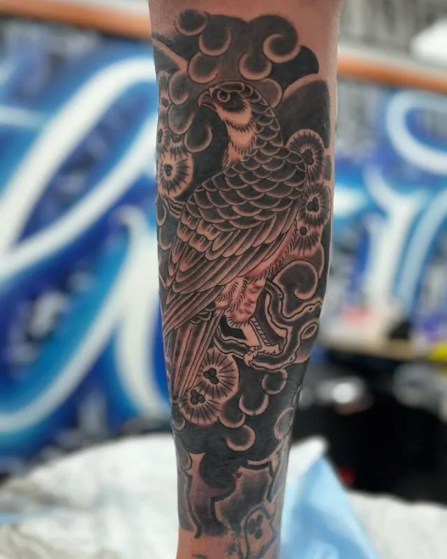Black and grey Japanese forearm sleeve tattoo of a hawk gripping a snake with chrysanthemum-burst clouds around it, by Franky Sharpz at Wailana Tattoo, Waikiki, Hawaii.