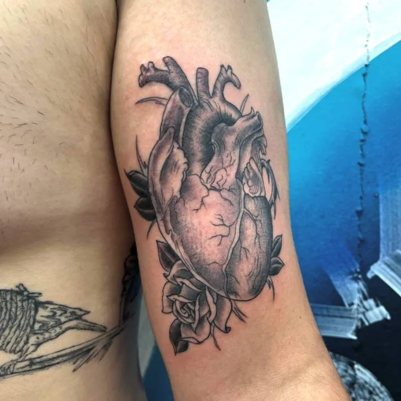 Black and grey tattoo of an anatomical heart with veins and a Traditional rose at the base, on the bicep, by Franky Sharpz at Wailana Tattoo, Waikiki, Hawaii.
