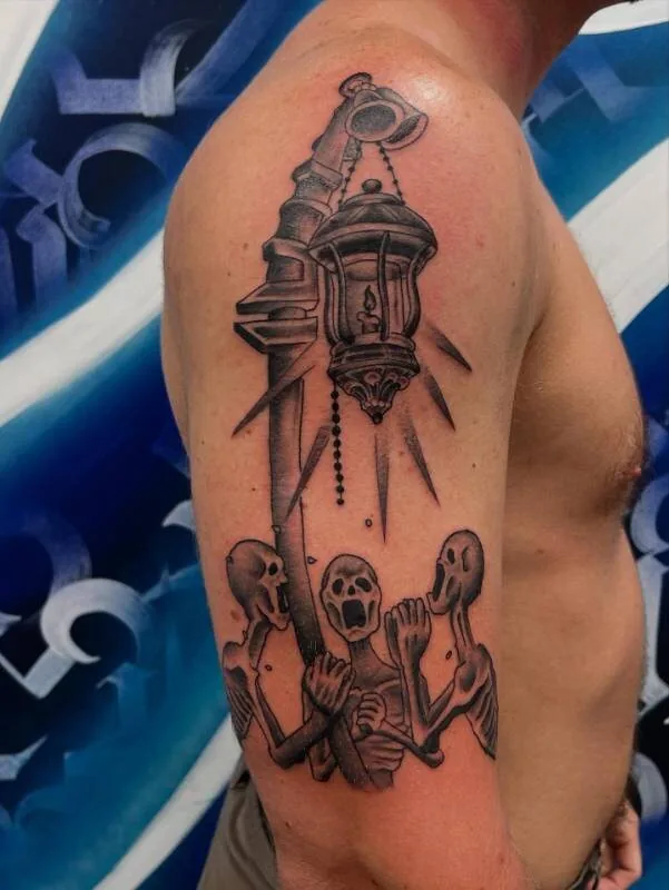 Black and grey surrealist tattoo of a Victorian street lantern with skeletal figures reaching up toward the light, on the upper arm, by Franky Sharpz at Wailana Tattoo, Waikiki, Hawaii.